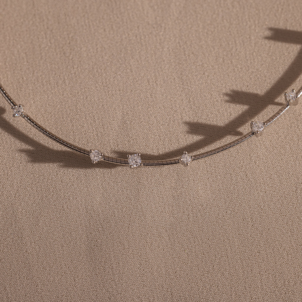 The Sprinkle Diamond Necklace features a delicate chain with evenly spaced clear gemstones, bringing everyday brilliance. Beautifully displayed on beige fabric.
