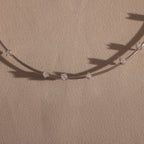 The Sprinkle Diamond Necklace features a delicate chain with evenly spaced clear gemstones, bringing everyday brilliance. Beautifully displayed on beige fabric.