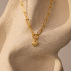 Paperclip Heart Charm Necklace in 18K Gold featuring a heart pendant, showcased on a textured beige sculpted surface.