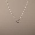 The Pearl Chain Clasp Necklace in Silver features a circular silver pendant with luminous pearls and is displayed on a plain beige background—an elegant addition to any jewelry collection.