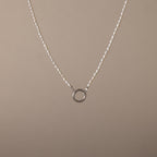 The Pearl Chain Clasp Necklace in Silver features a circular silver pendant with luminous pearls and is displayed on a plain beige background—an elegant addition to any jewelry collection.