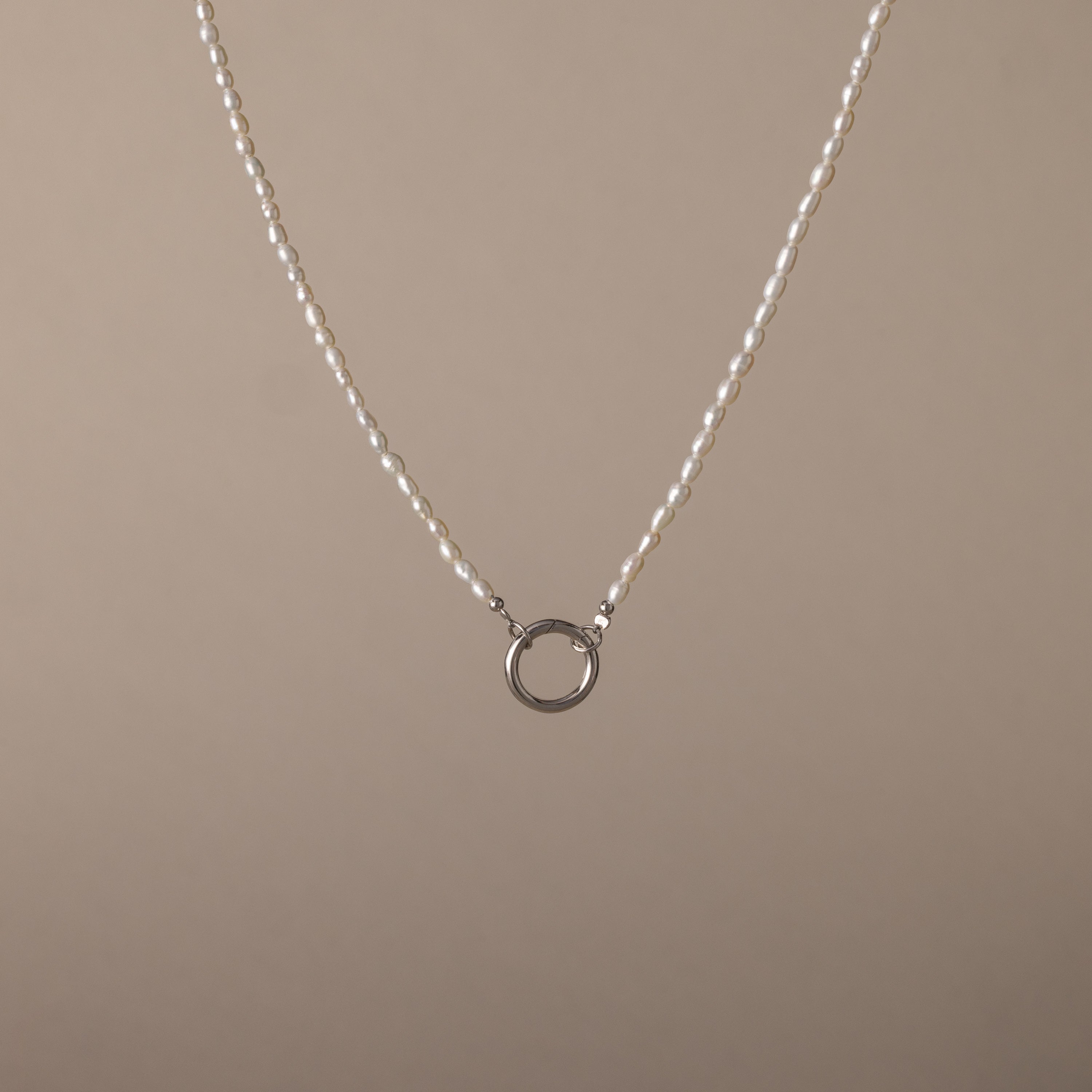 The Pearl Chain Clasp Necklace in Silver features a circular silver pendant with luminous pearls and is displayed on a plain beige background—an elegant addition to any jewelry collection.