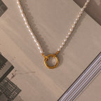 The Pearl Chain Clasp Necklace in 18K Gold, featuring a gold circular pendant, is displayed on an open book with a cityscape—an elegant and timeless addition to your jewelry collection.