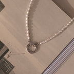 The Pearl Chain Clasp Necklace in Silver, featuring luminous pearls, is displayed on an open book with architectural images—an elegant addition to any jewelry collection.