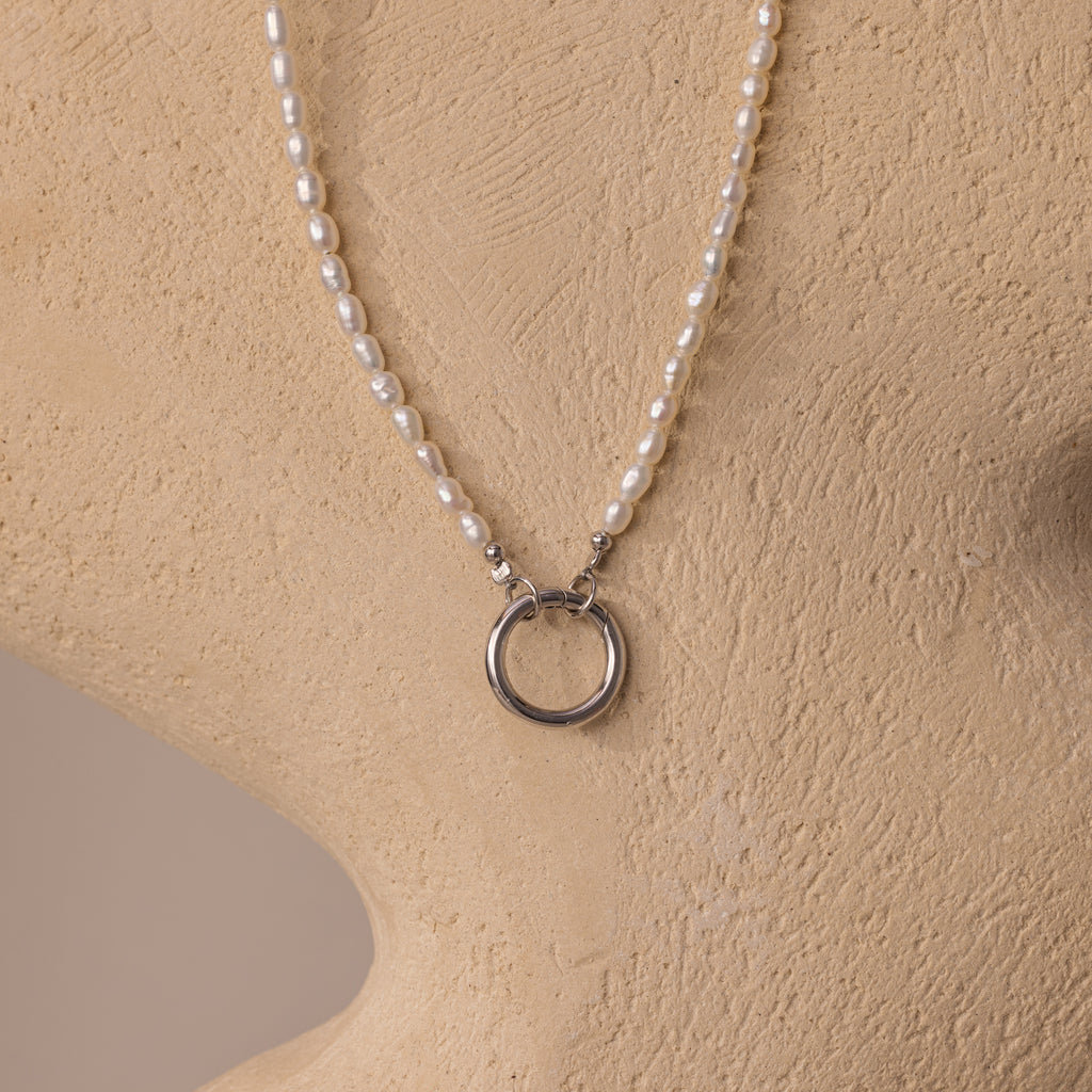 The Pearl Chain Clasp Necklace in Silver, from our jewelry collection, features luminous pearls and a silver ring pendant, elegantly displayed on a beige mannequin bust.
