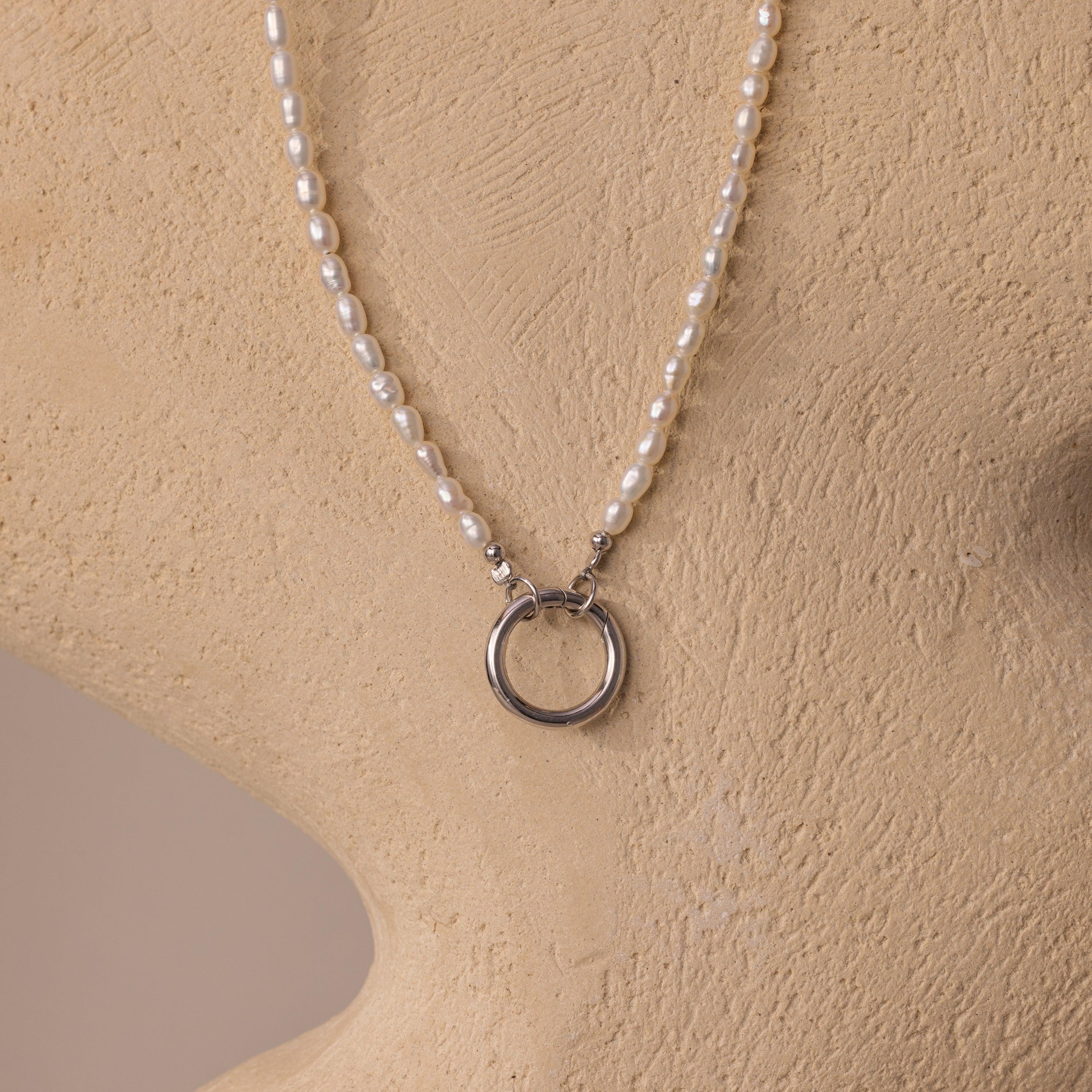 The Pearl Chain Clasp Necklace in Silver, from our jewelry collection, features luminous pearls and a silver ring pendant, elegantly displayed on a beige mannequin bust.