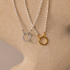 Two Pearl Chain Clasp Necklaces, each with silver and gold circular pendants, are displayed on a beige textured mannequin—a modern accessory perfect for any occasion.