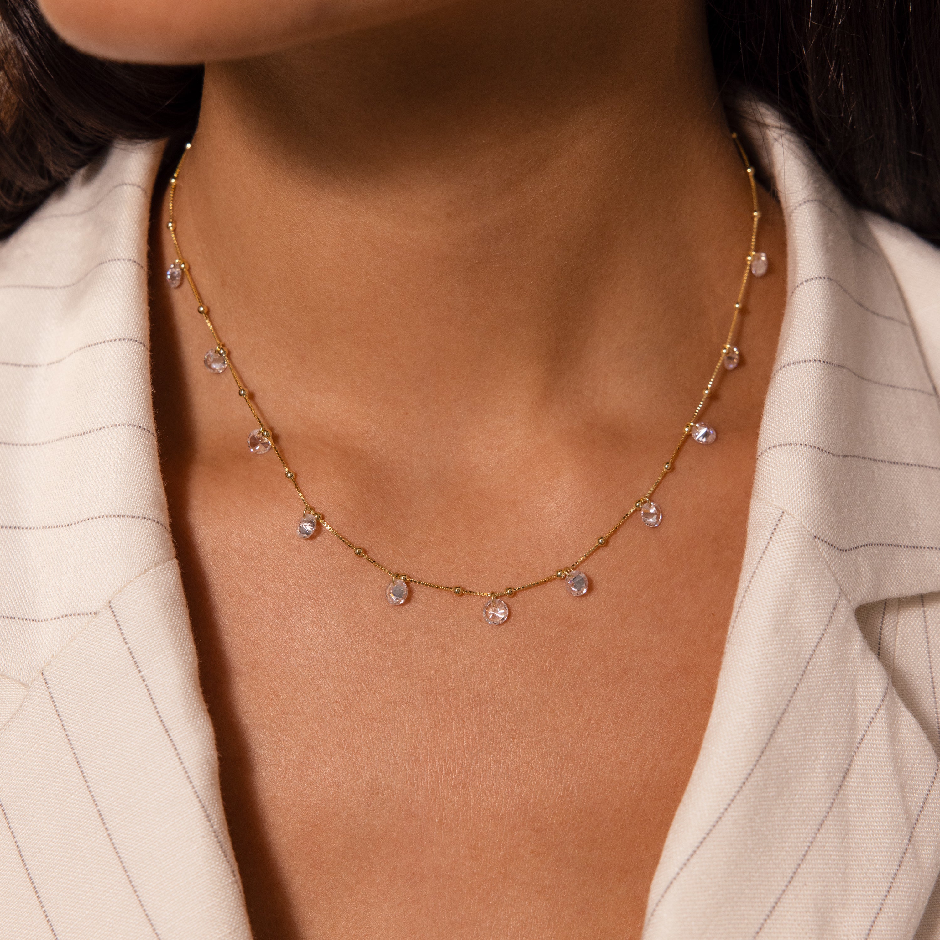 Close-up of a woman wearing the Satellite Diamond Necklace with delicate gemstone charms, paired with a cream pinstripe blazer.