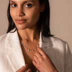 A woman in a white pinstripe blazer wears the Satellite Diamond Necklace in Silver, looking at the camera with a slight smile.