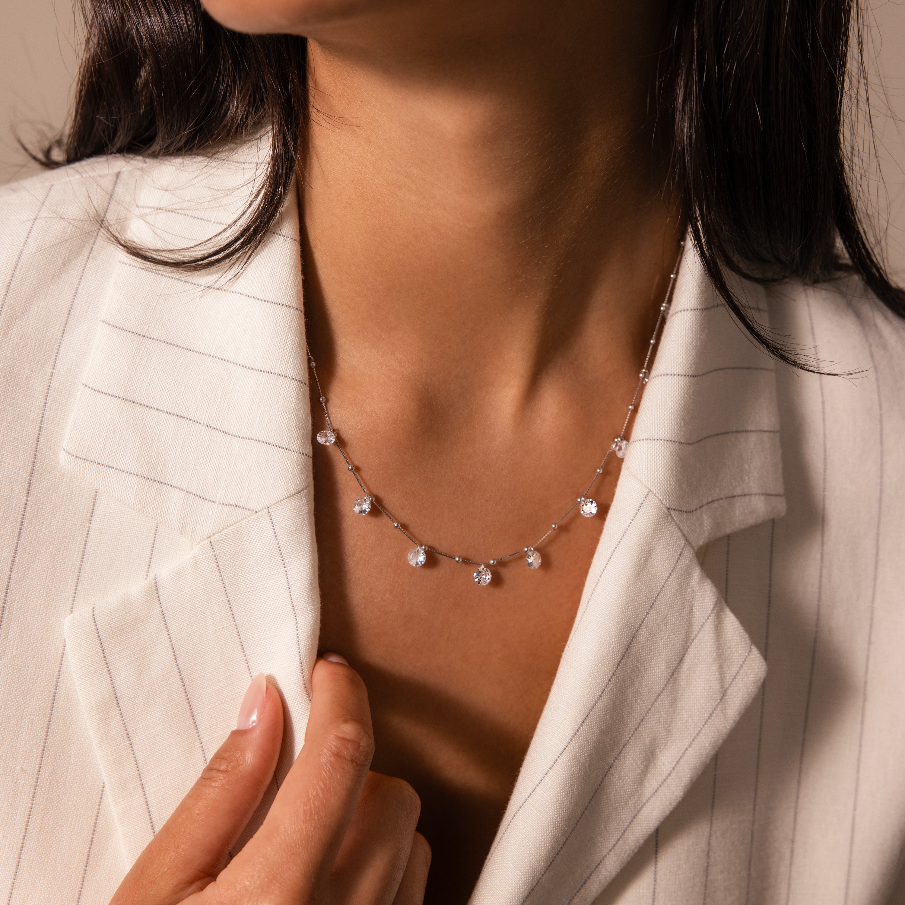 A woman in a white pinstripe blazer wears the Satellite Diamond Necklace in Silver—a dainty necklace accented with small, sparkling gems.
