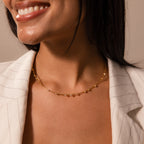 A woman in a cream blazer smiles, wearing a delicate chain layering necklace and the Sprinkle Diamond Necklace in 18K Gold adorned with small charms.