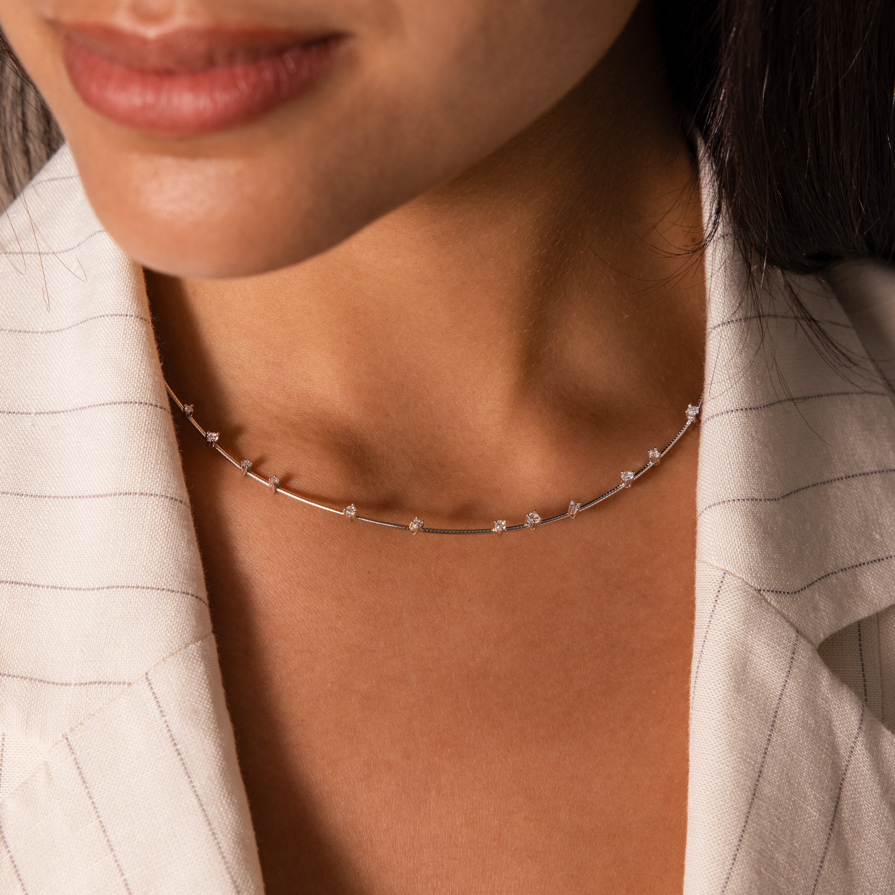 A woman wears the Sprinkle Diamond Necklace, its delicate chain and small gemstones adding everyday brilliance to her look, paired with a light striped blazer.