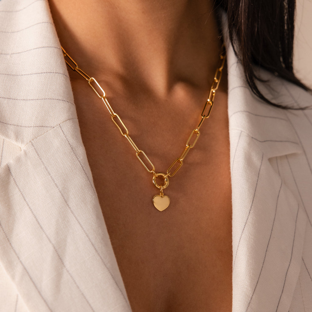 A woman wearing the Paperclip Heart Charm Necklace in 18K Gold with a heart pendant over a white pinstripe blazer.