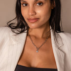 A woman smiles softly at the camera, wearing a white blazer and the Paperclip Heart Charm Necklace in Silver.