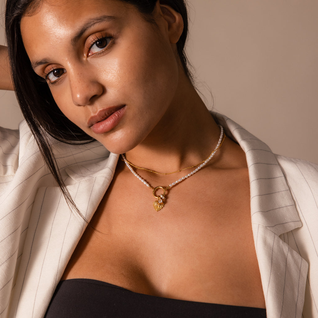 Woman in a pinstripe blazer wears the Pearl Chain Clasp Necklace in 18K Gold, gazing at the camera with a neutral expression—a sophisticated piece to elevate any jewelry collection.