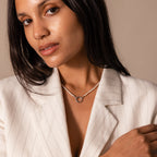 A woman in a white pinstripe blazer wears the Pearl Chain Clasp Necklace in Silver with a round pendant, posing against a beige background.