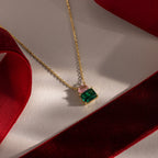 Flatlay of our Emerald Bloom Necklace with Pink Tourmaline and Emerald Gemstones against red ribbons