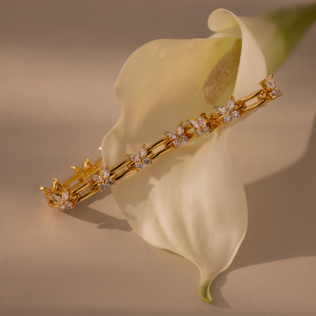 The Mariposa Link Bracelet, crafted in gold with diamonds and shaped like butterflies, is elegantly displayed on a white calla lily flower, highlighting the refined beauty of feminine jewelry.