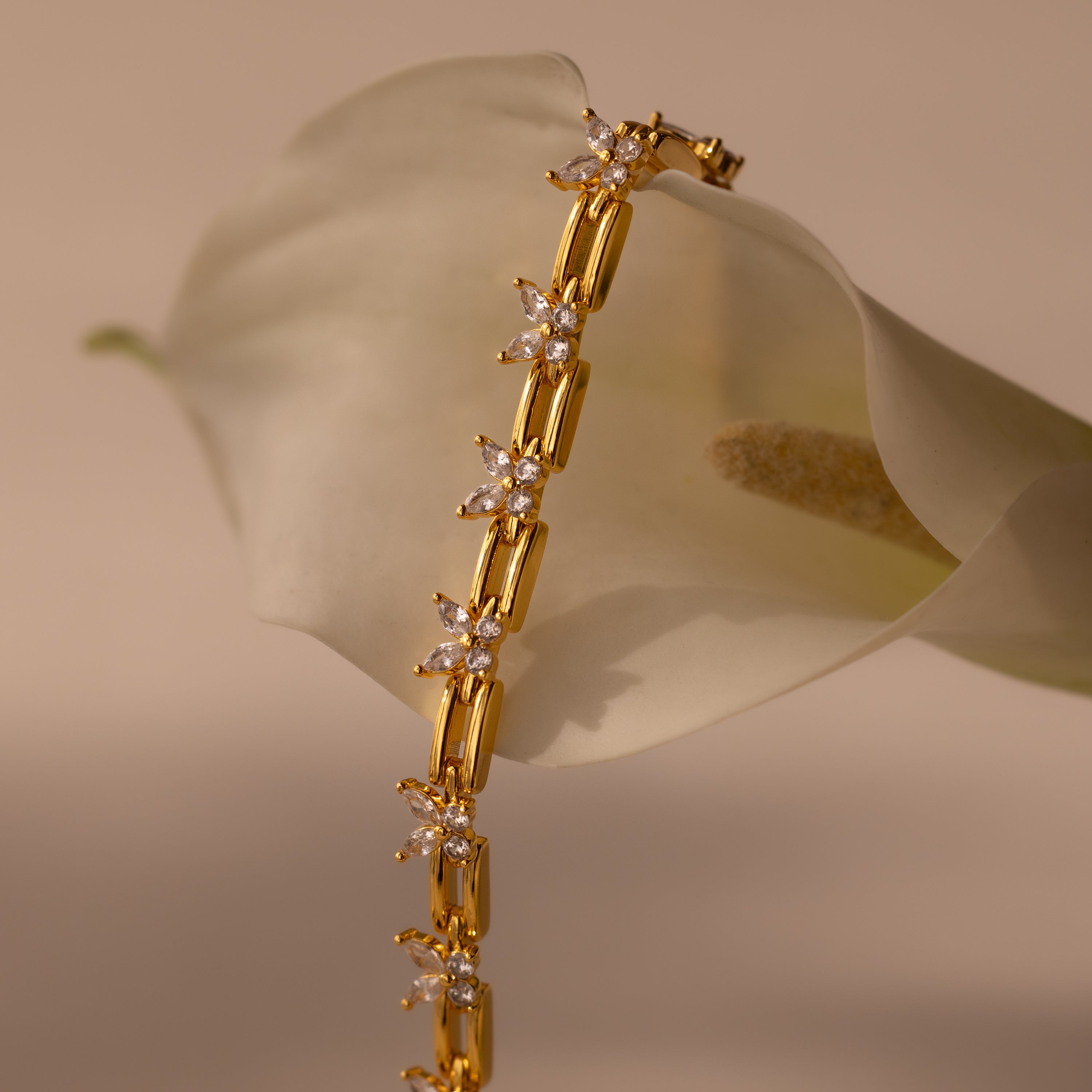 The Mariposa Link Bracelet, adorned with star-shaped accents and diamonds, drapes elegantly over a white calla lily—an ideal choice for those who love feminine jewelry.