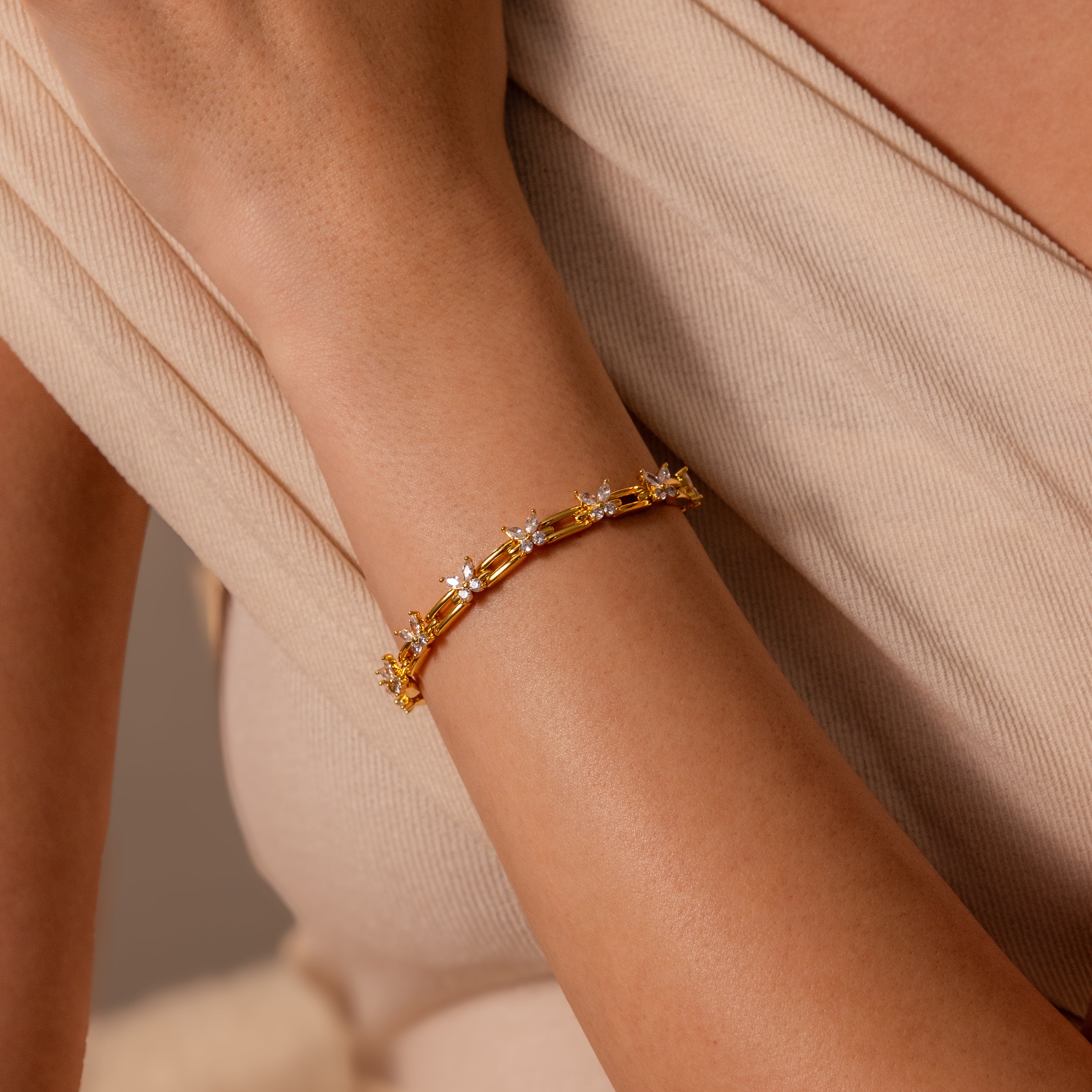 The Mariposa Link Bracelet, adorned with star-shaped charms, adds a feminine touch to a woman’s wrist against a beige, textured fabric background.