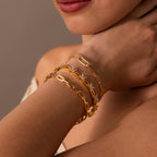 A woman's hand near her face showcases the Mariposa Link Bracelet—a gold butterfly design paired with two elegant gold bracelets for a refined, feminine look.