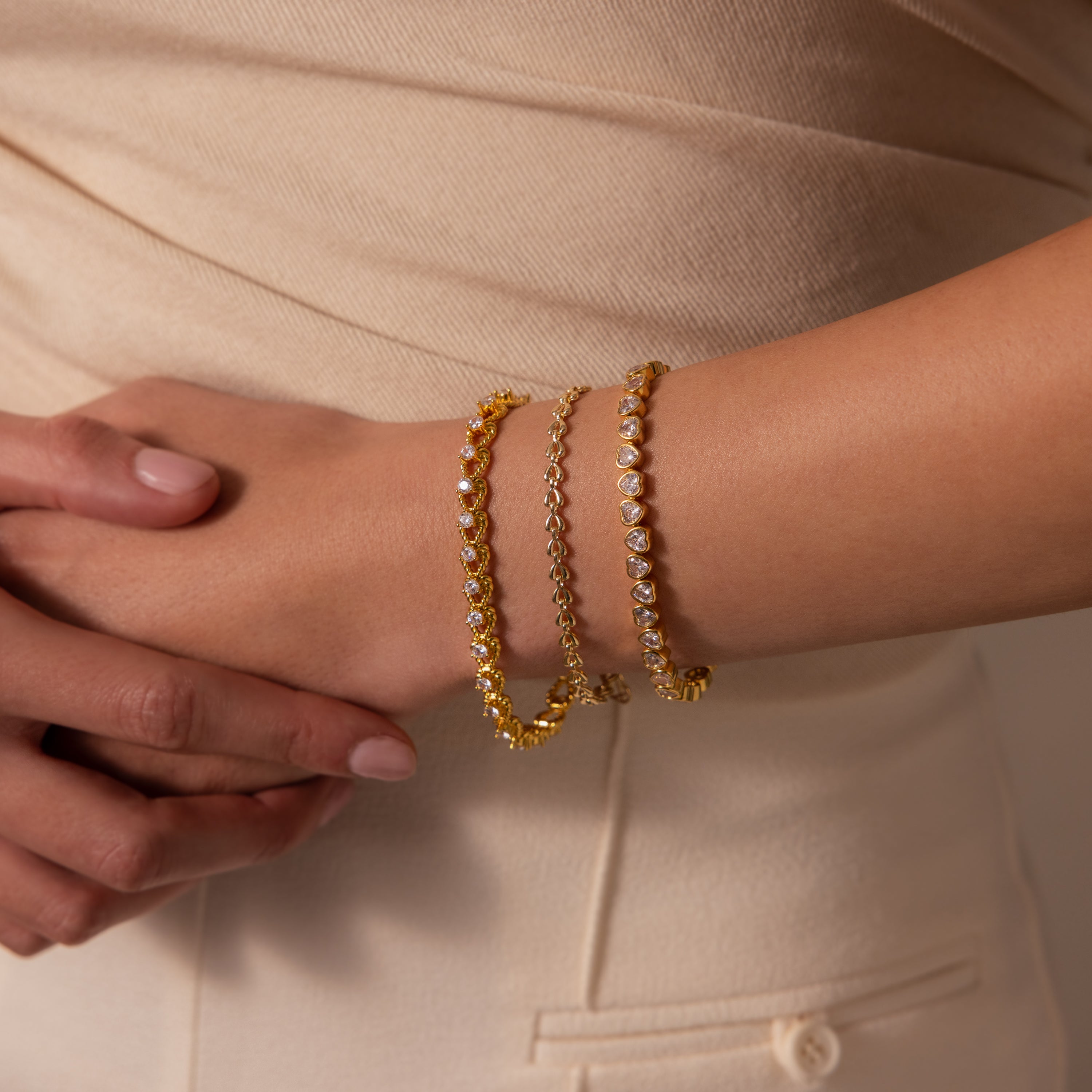 A person wearing an elegant Heart Tennis Bracelet and cream-colored clothing rests their hand on their hip.