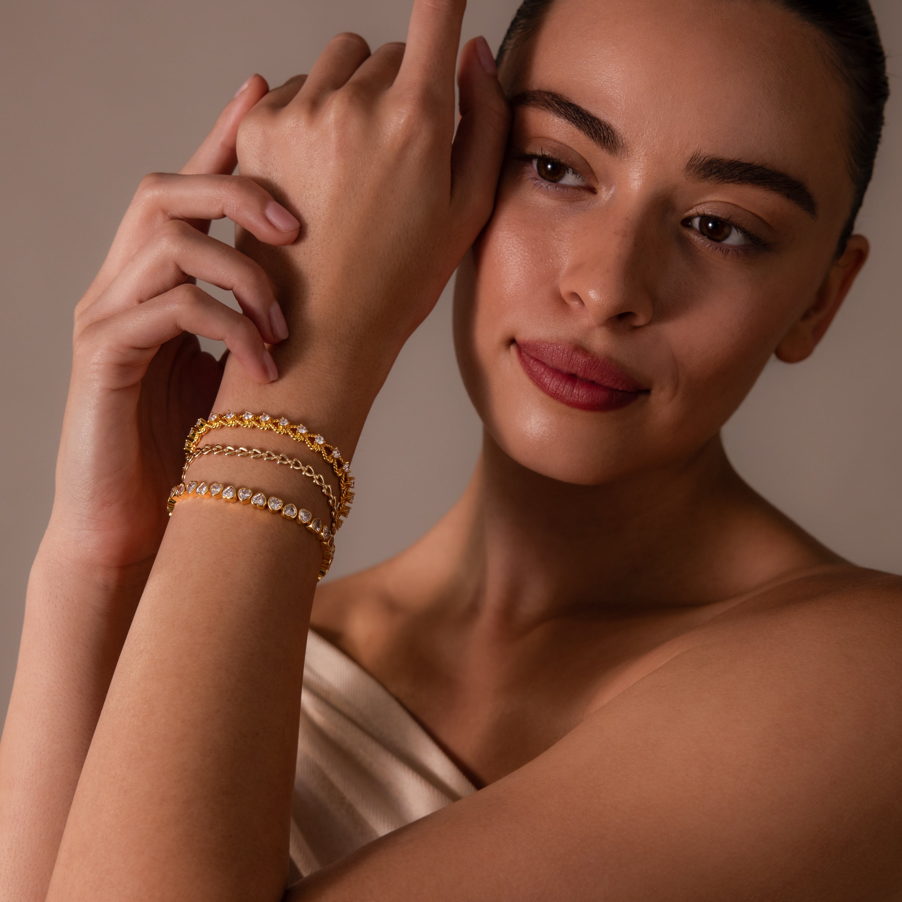 A woman with a soft expression poses with one arm raised, showcasing the Diamond Heart Rope Bracelet along with gold bracelets.