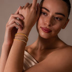 A woman wearing an off-shoulder top elegantly showcases the Heart Tennis Bracelet with heart-shaped stones on her wrist, glancing to the side with a gentle smile.