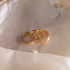 The Pave Birthstone Charm Clip shines with colorful gemstones, displayed on a smooth, iridescent shell surface.