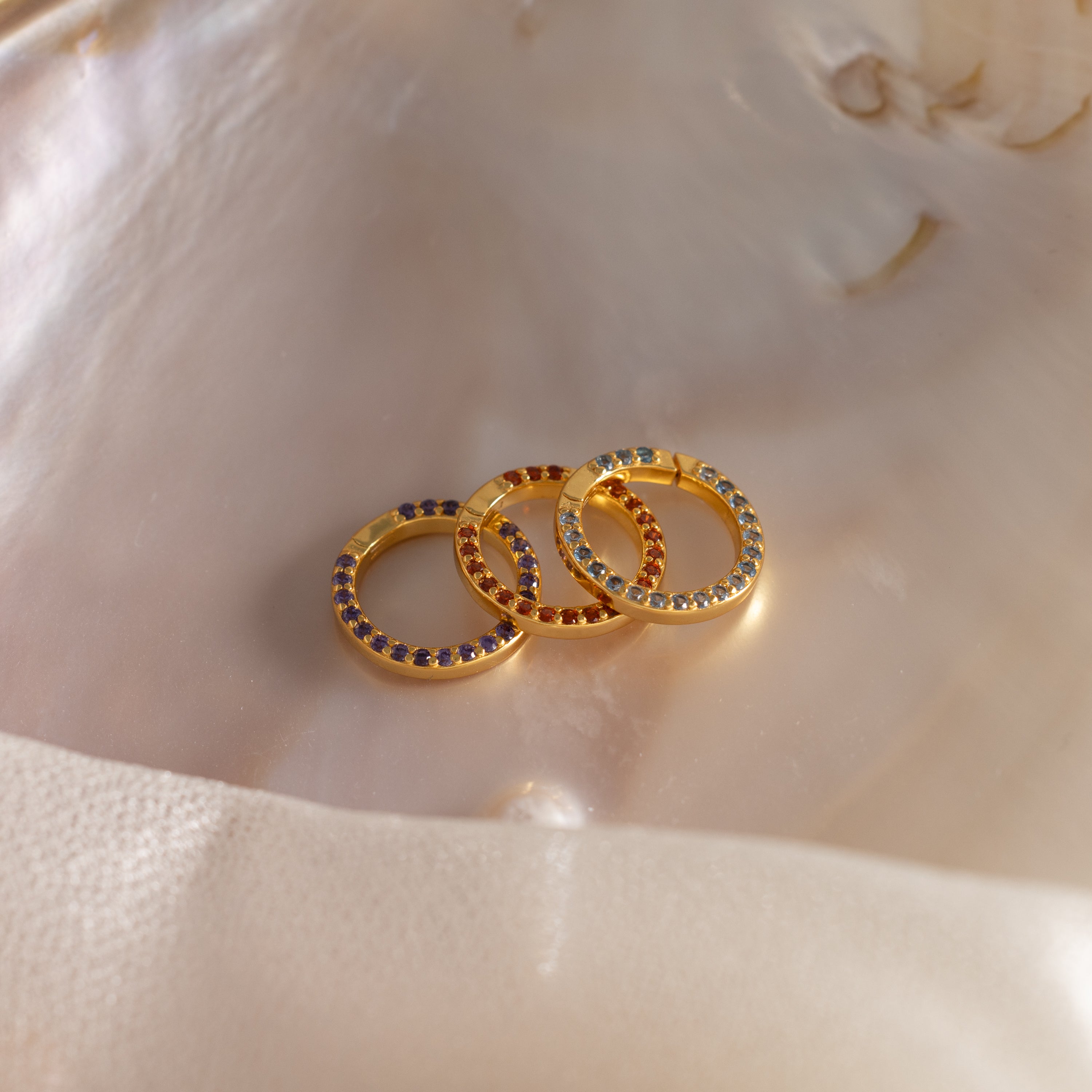 The Pave Birthstone Charm Clip shines with colorful gemstones, displayed on a smooth, iridescent shell surface.