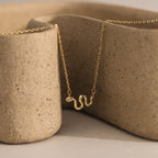 Close-up of a gold viper snake pendant necklace with pavé accents, displayed against a textured ceramic background.