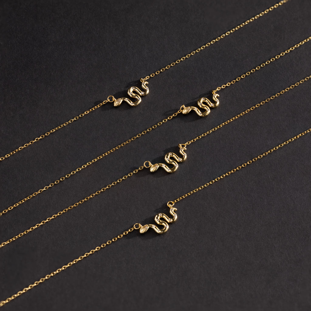 Flat lay of 4 dainty gold viper necklaces featuring curved snake pendants on delicate chains.