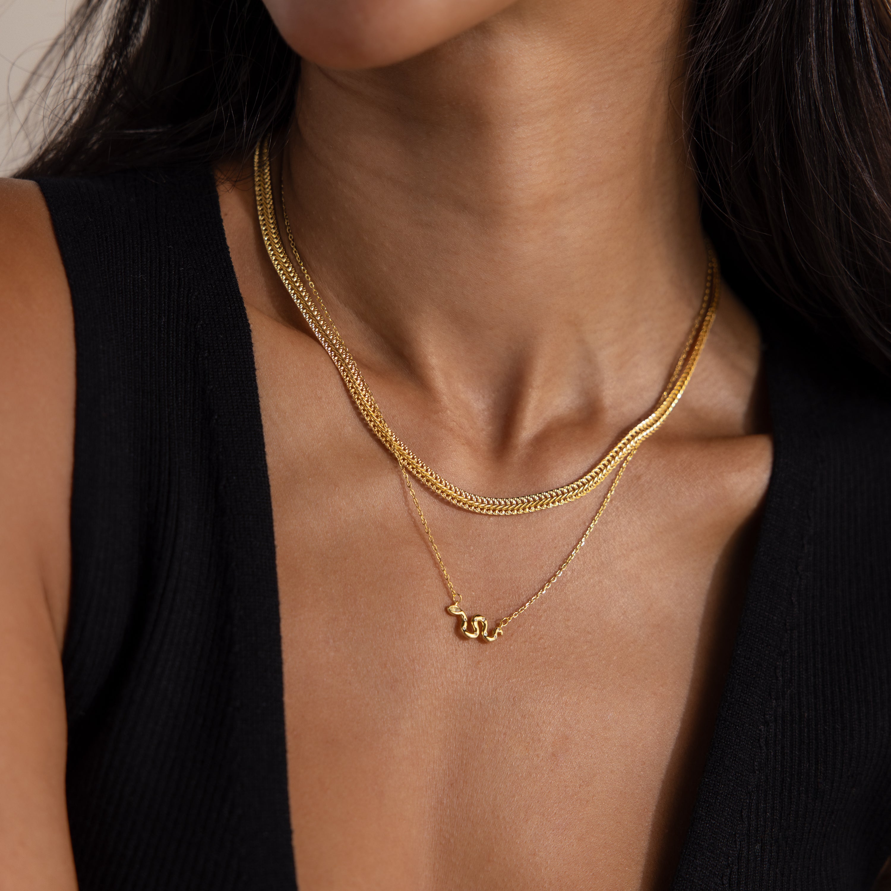 Layered gold chain necklaces styled on a woman, highlighting a minimalist snake pendant on the shortest chain.