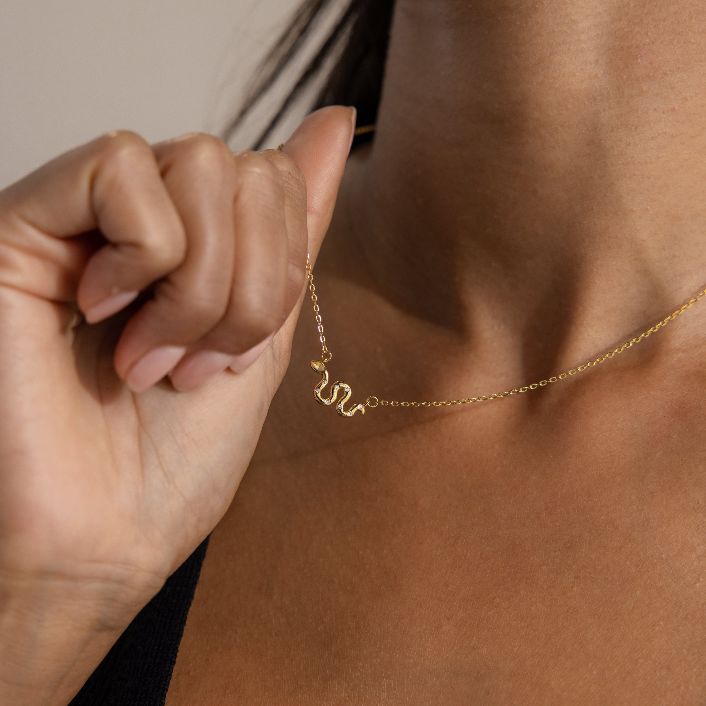 Model gently lifting a dainty gold serpent charm necklace with a pavé-detailed snake pendant.
