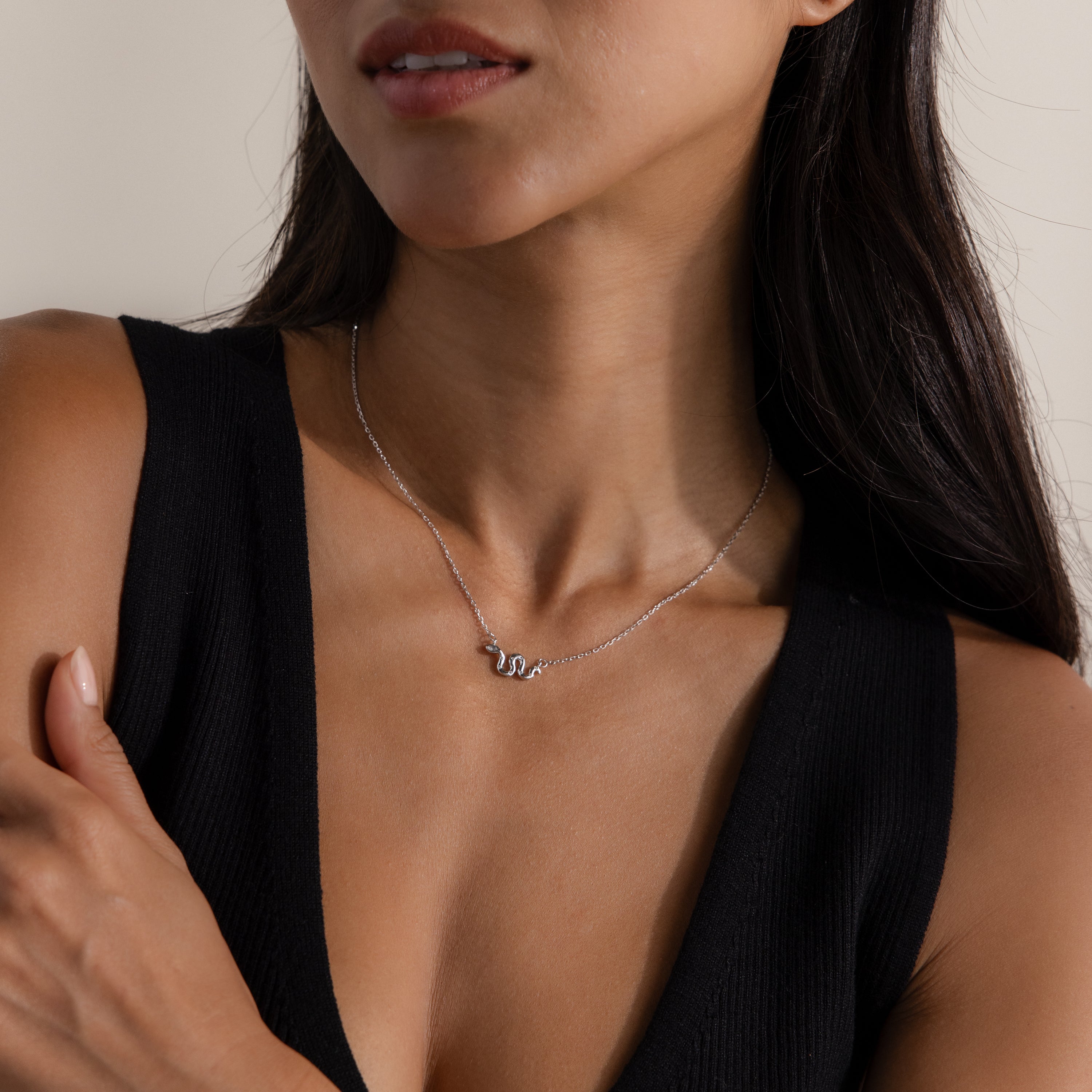 Close-up of a silver viper snake charm necklace on a model in a black v-neck top.