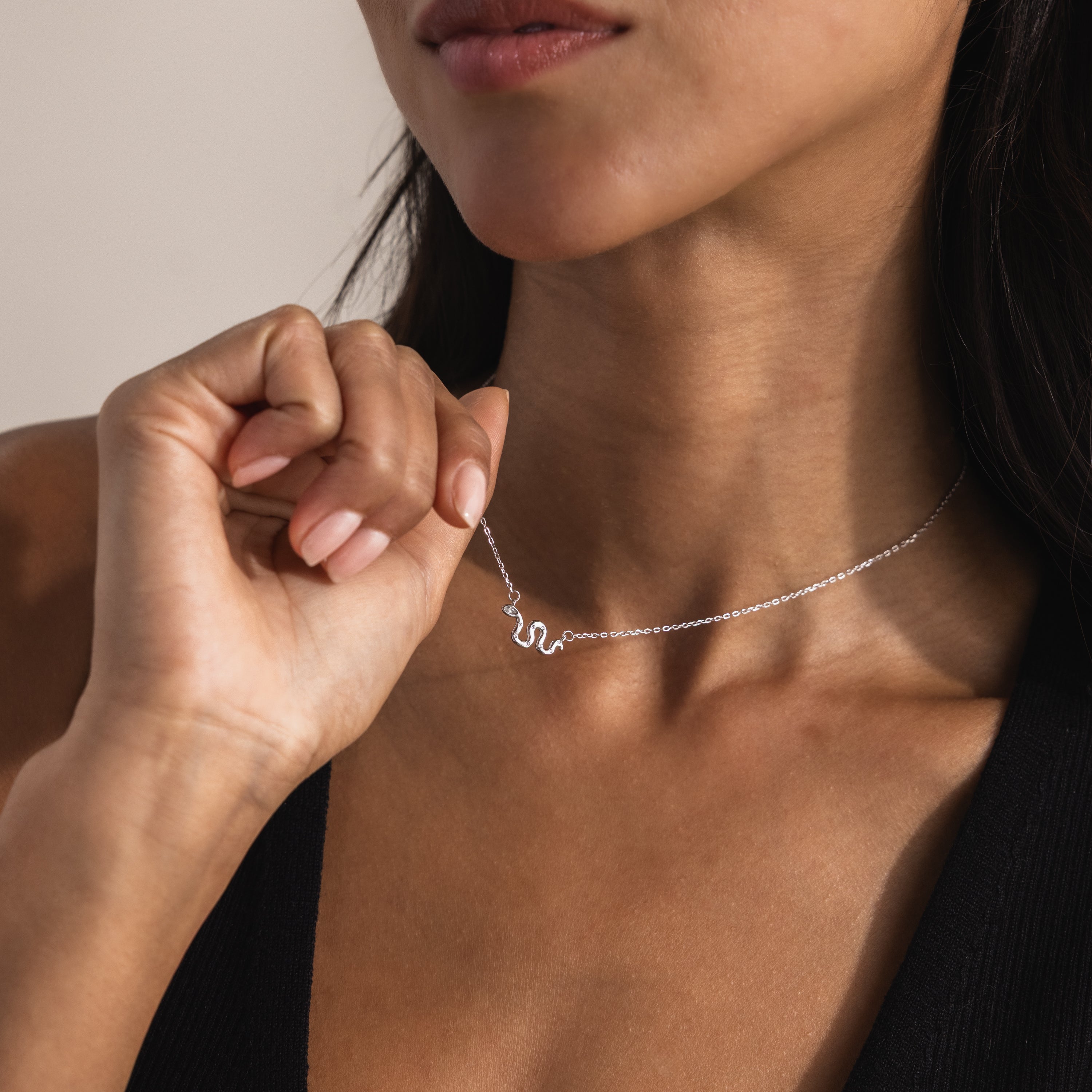 Close-up of a model gently lifting a dainty silver viper snake charm necklace with a minimalist cable chain.