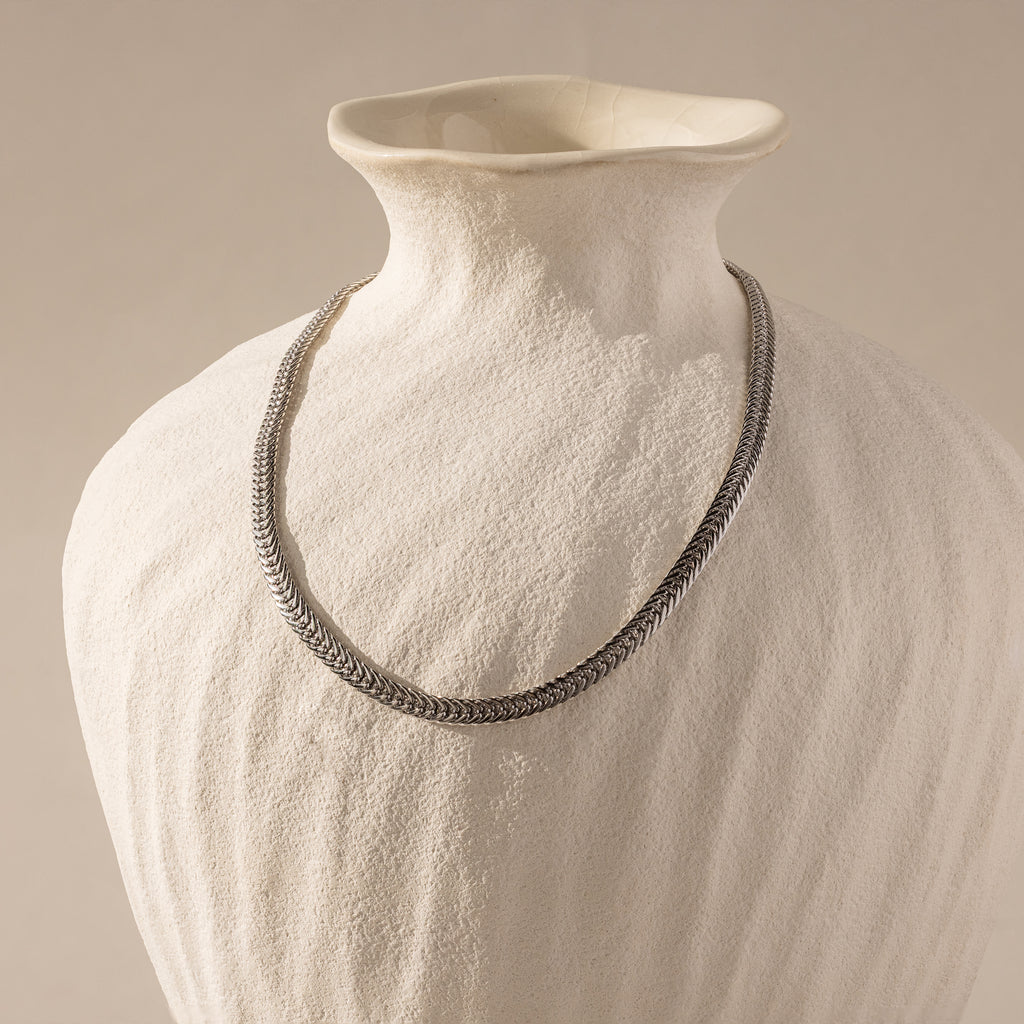 The Thick Mesh Chain Necklace is showcased draped over a textured white ceramic vase, set against a neutral background.