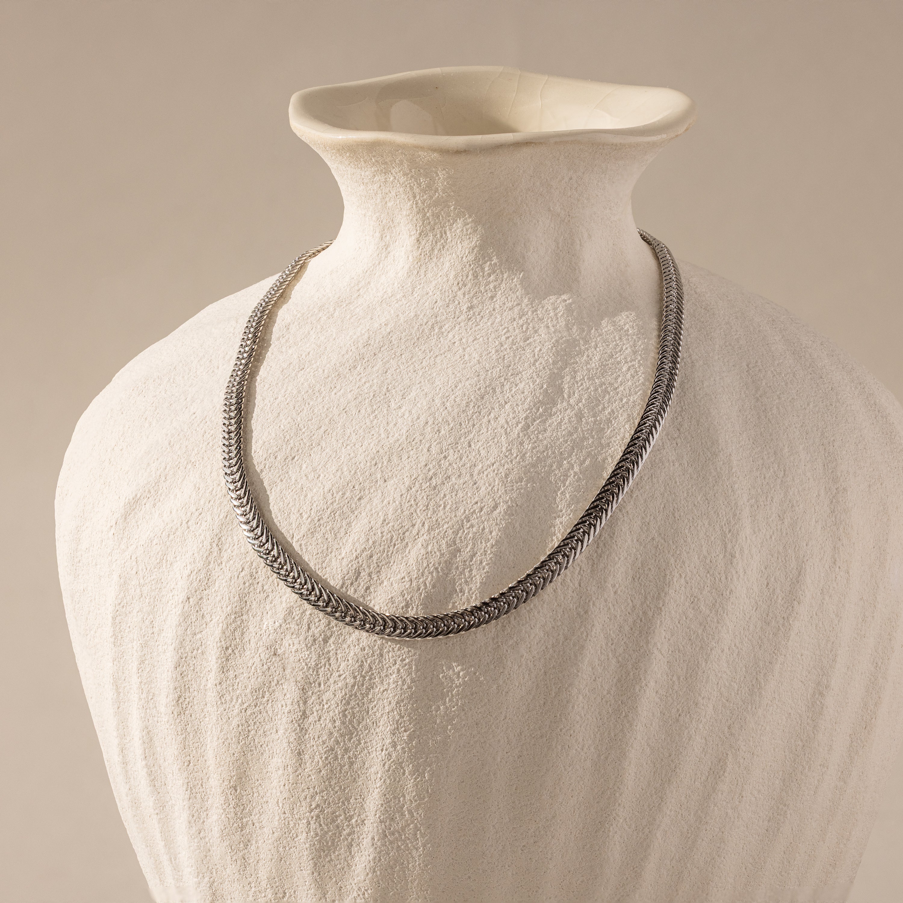 The Thick Mesh Chain Necklace is showcased draped over a textured white ceramic vase, set against a neutral background.