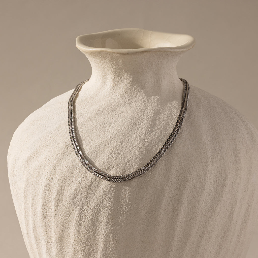 The gold mesh necklace displayed on a matte ceramic bust.