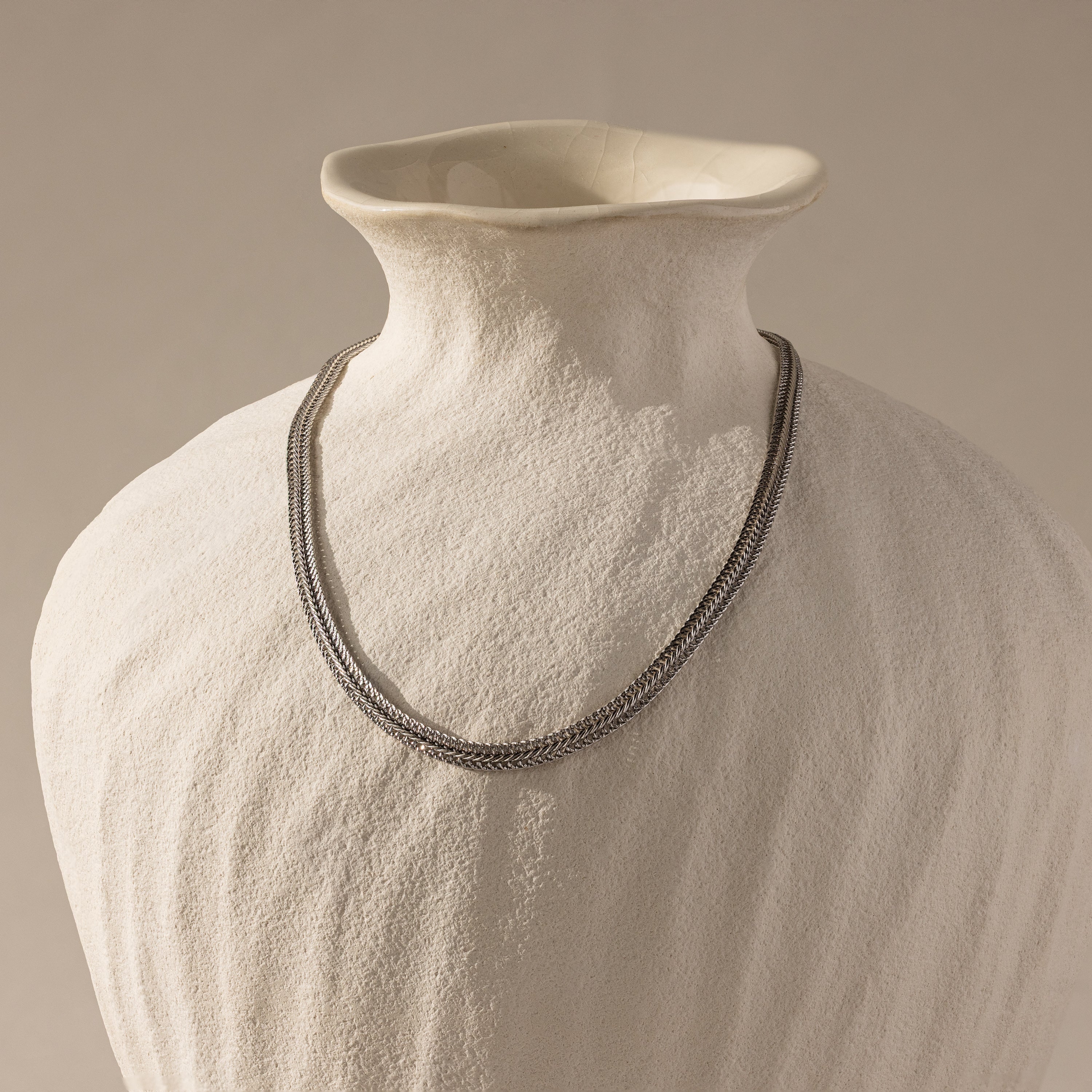 The gold mesh necklace displayed on a matte ceramic bust.