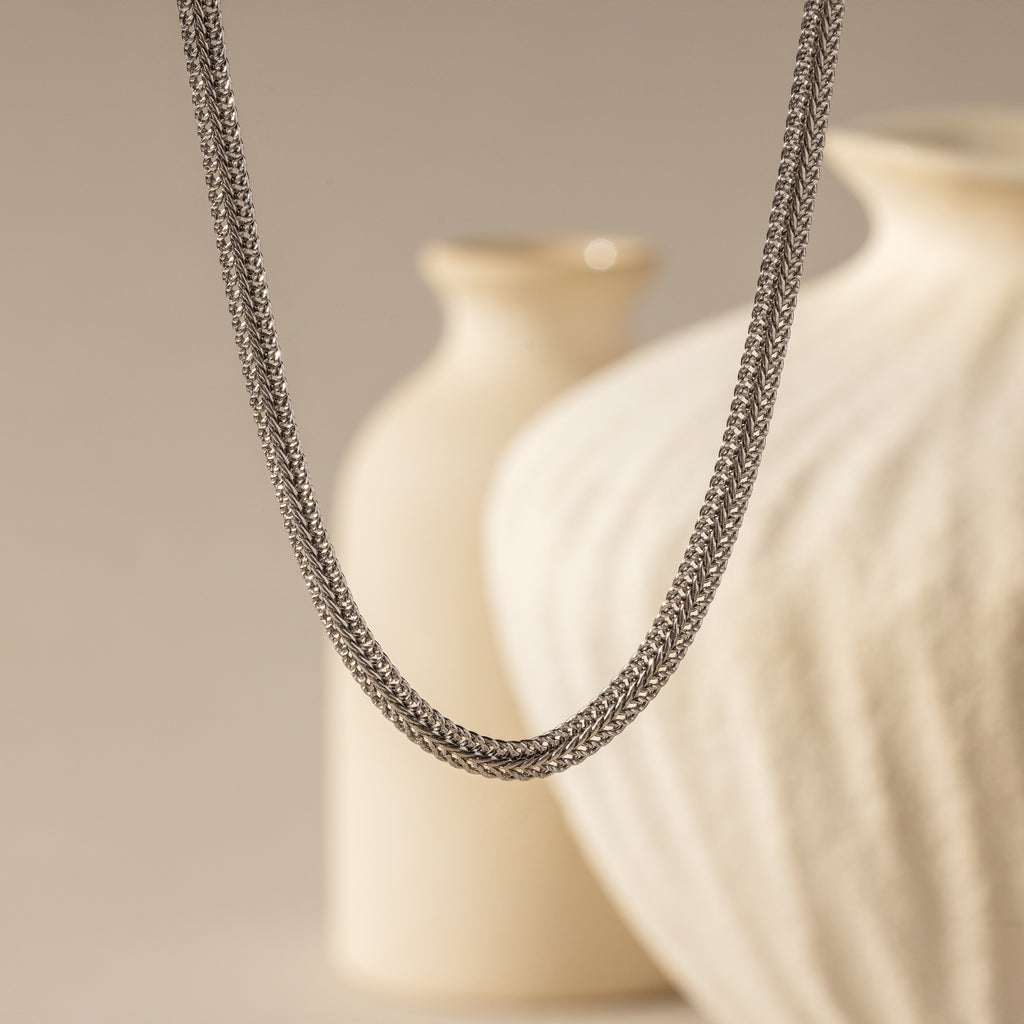 hick Mesh Chain Necklace in silver floats against a soft neutral backdrop. The lighting enhances the tightly interlocked mesh links, showcasing the necklace’s uniform weave