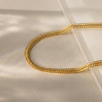 Close-up of a gold mesh chain necklace with intricate woven texture, displayed on a neutral background with soft lighting.