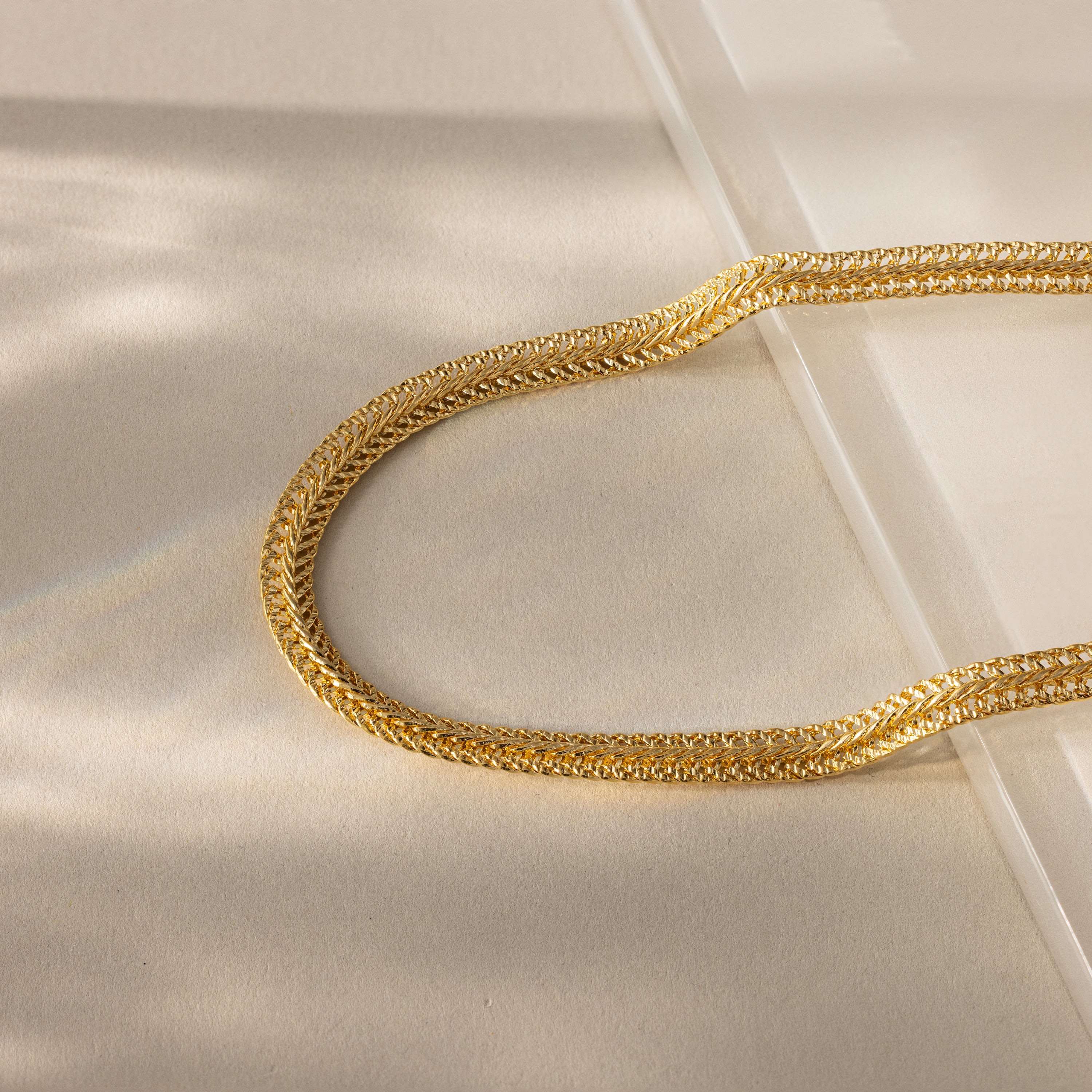 Close-up of a gold mesh chain necklace with intricate woven texture, displayed on a neutral background with soft lighting.