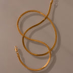 The Twisted Snake Chain Necklace in 18K Gold, featuring a lobster clasp and arranged in loose curves on a neutral background, is perfect as modern jewelry and ideal for layering.
