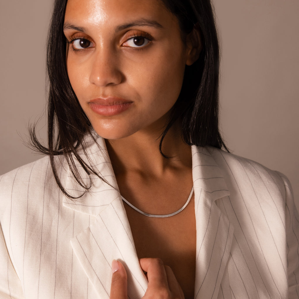 A woman wearing a white pinstripe blazer and the Twisted Snake Chain Necklace in Silver looks at the camera with a neutral expression.