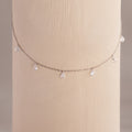 Diamond teardrop station necklace in silver draped around a textured cylindrical display in soft lighting.