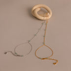 The Jade Hand Chain Bracelet in 18K Gold is elegantly displayed on a beige twisted ceramic holder.