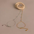 The Jade Hand Chain Bracelet is a delicate piece featuring small green jade beads and a heart clasp, available in gold or silver chains, shown on a beige background.