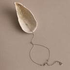 The Jade Hand Chain Bracelet features delicate silver and green jade beads, beautifully presented on a cream-colored shell.