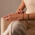 A person in cream clothing showcases the Jade Hand Chain Bracelet in 18K Gold, featuring delicate green jade beads and a gold hand chain on their wrist and hand.